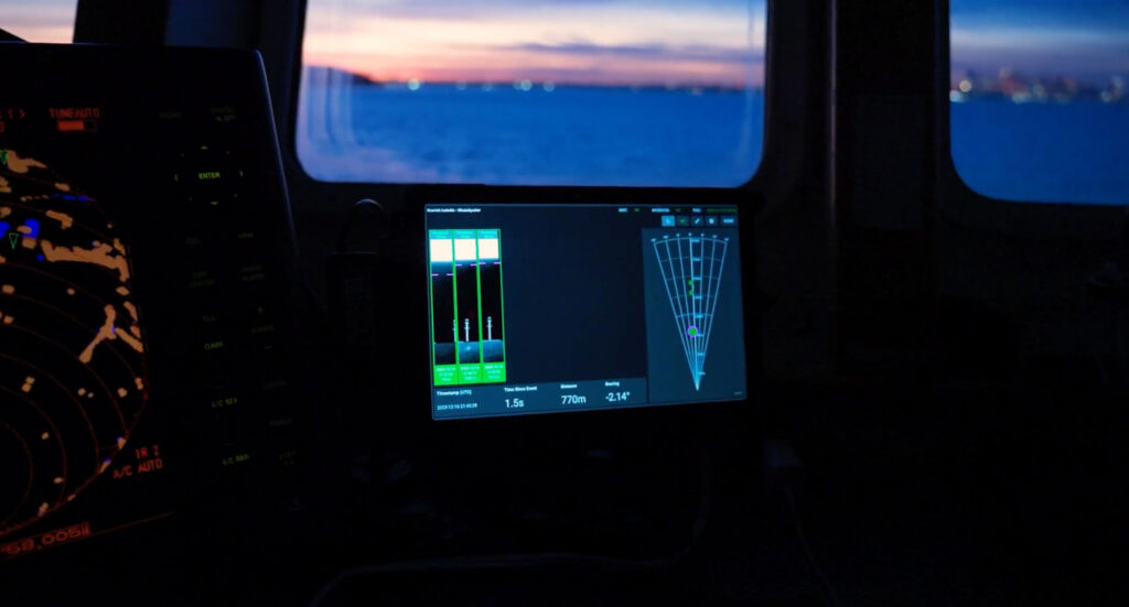 View from inside a boat at dusk showing navigation and sonar screens glowing in the cabin, with open water visible through the windows.